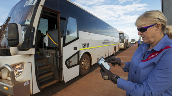 Sodexo Mitarbeiterin hält Tablet in der Hand mit einem Bus im Hintergrund