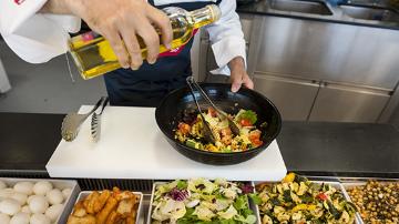 Koch bereitet frisch einen Salat zu und hält Olivenöl in seiner linken Hand, welches er zu dem Salat hinzufügt