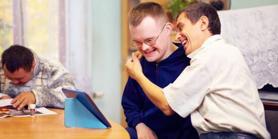 deux jeunes handicapés se serrent dans les bras et regardent une tablette