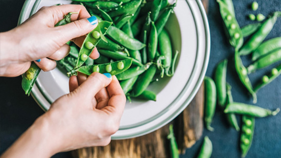 Zoom sur des main décortiquant des petits pois