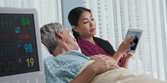 woman  with a tablet in hand talking to a man lying in a hospital bed