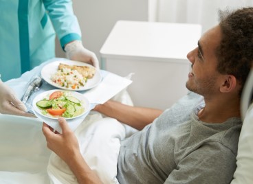 a person in a hospital bed holding plates of food