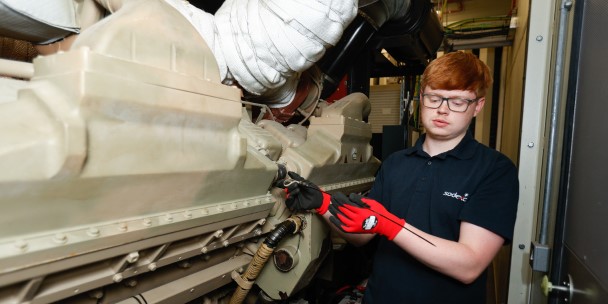 A young man in a black shirt intently working on a large engine,