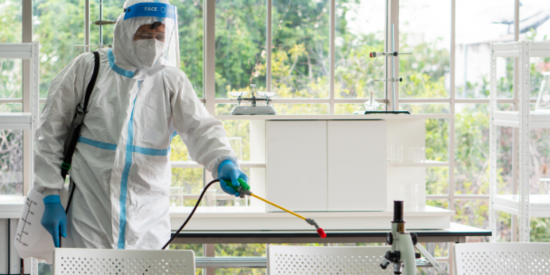 A man wearing a white suit and mask disinfecting a laboratory