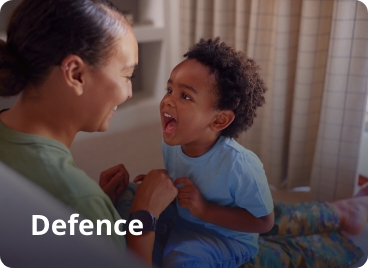 A woman and child sitting on a couch and smiling. Word on the image says Defence