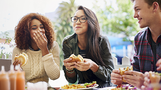 Three students eating burgers and smiling