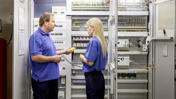 A male and a female sodexo employee standing in front of a cupboard full of switches