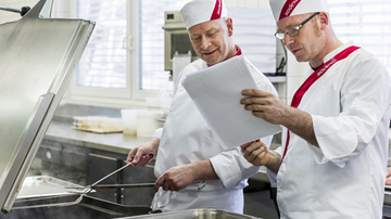 Two chefs reading notes in a kitchen