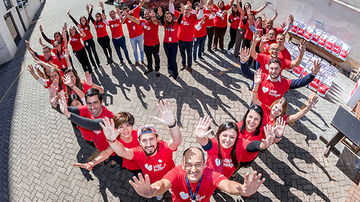 Group of people wearing stop hunger t-shirts standing in the shape of a heart and waving