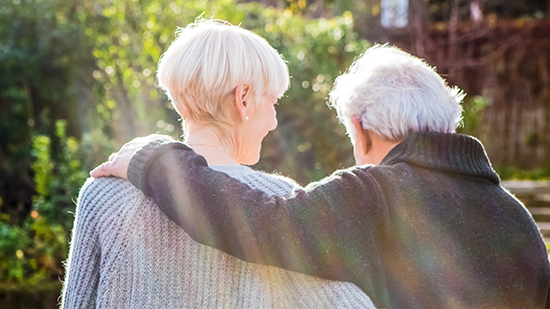 A male and female elderly person hugging each other, view from behind