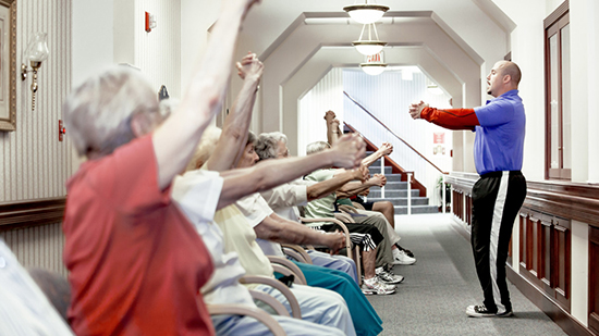 A sodexo employee running an exercise to a row of seated elderly people