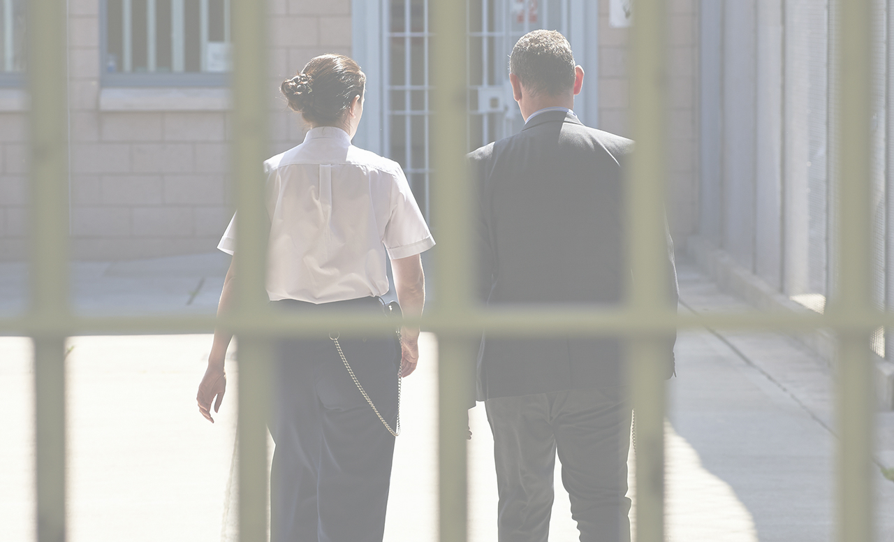 A male and a female prison officer walking through a prison, prison bars in the foreground