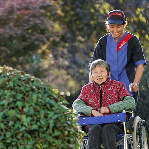 Sodexo nurse pushing elderly woman in a wheelchair through a garden